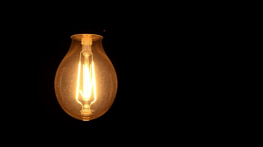 Glowing vintage light bulb with inventor silhouettes.